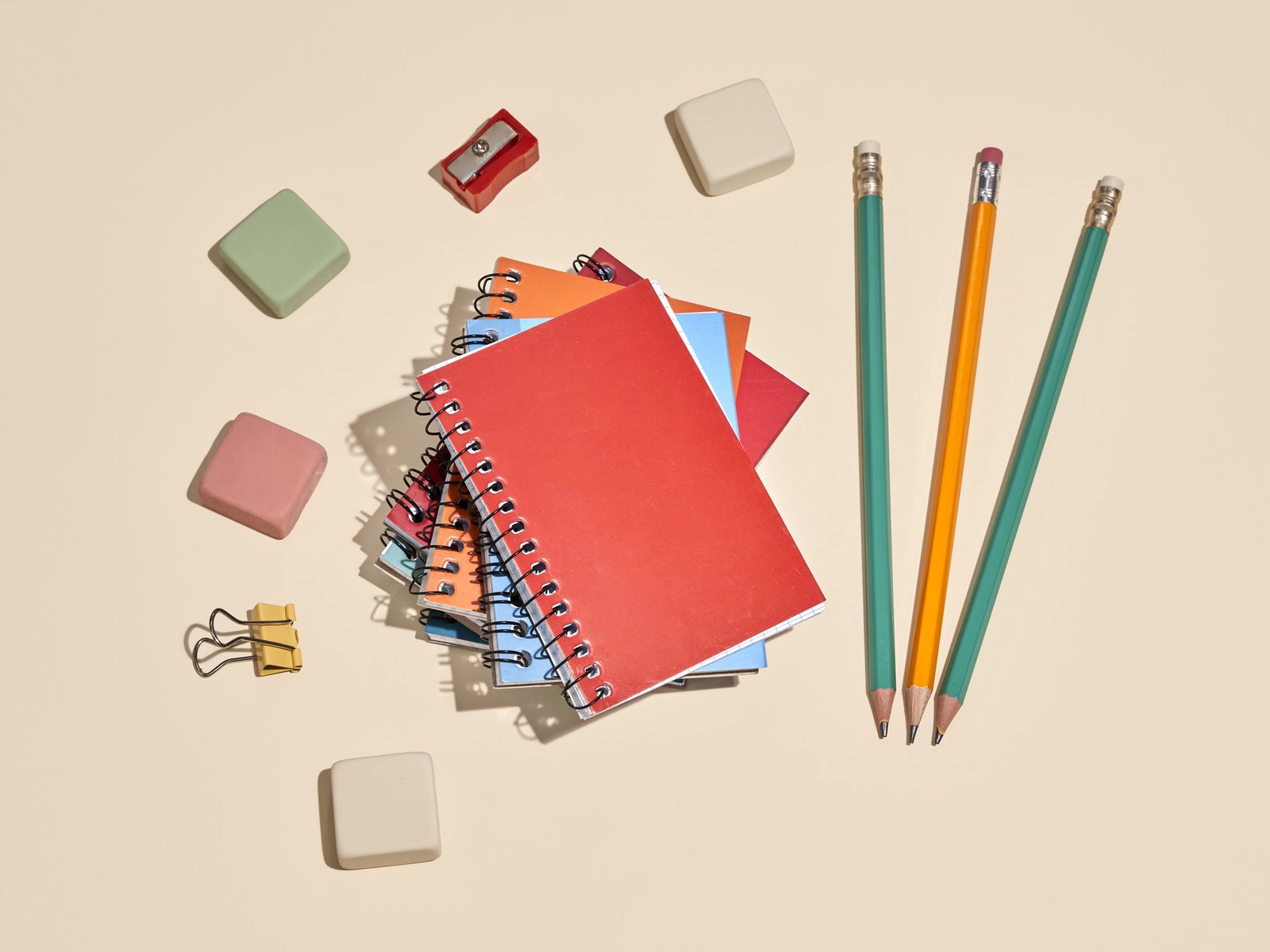 School supplies including notebooks erasers and pencils laid out on a beige backdrop
